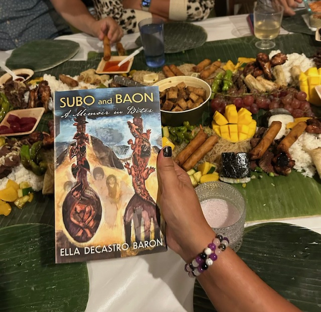 Image of book, Subo and Baon: a Memoir in Bites, by Ella deCastro Baron, in front of a kamayan-style food spread